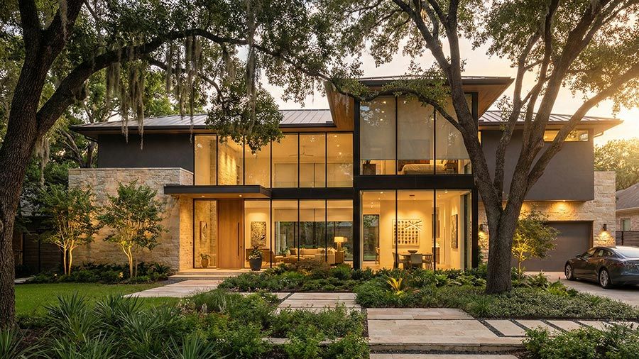 Contemporary two story home with glass walls and lush front landscaping
