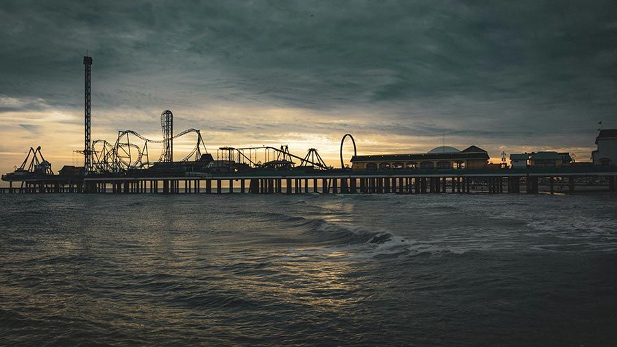 Pier with amusement rides at sunset over the ocean