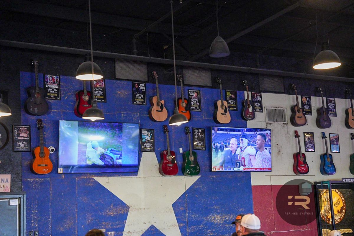 Wall with mounted TVs, guitars, and event posters in a music-themed sports bar.
