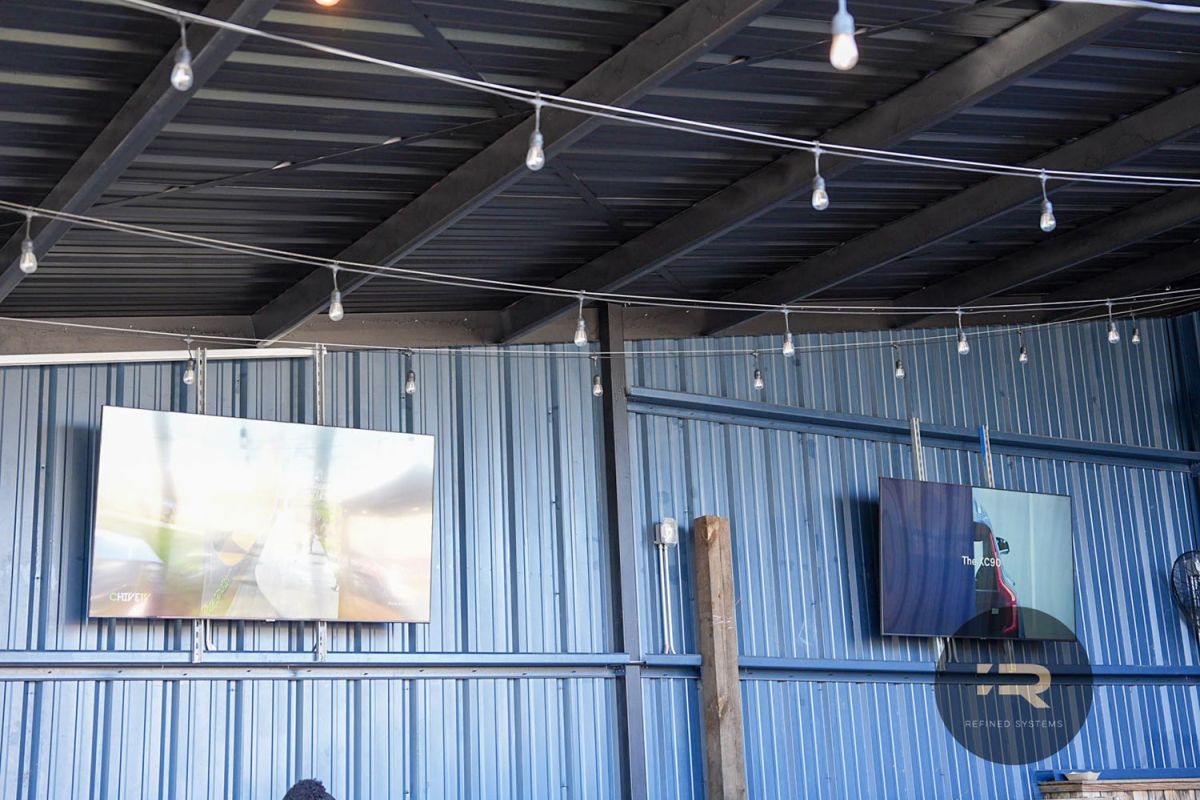 Wall-mounted TVs on a covered patio with string lights and a metal ceiling.