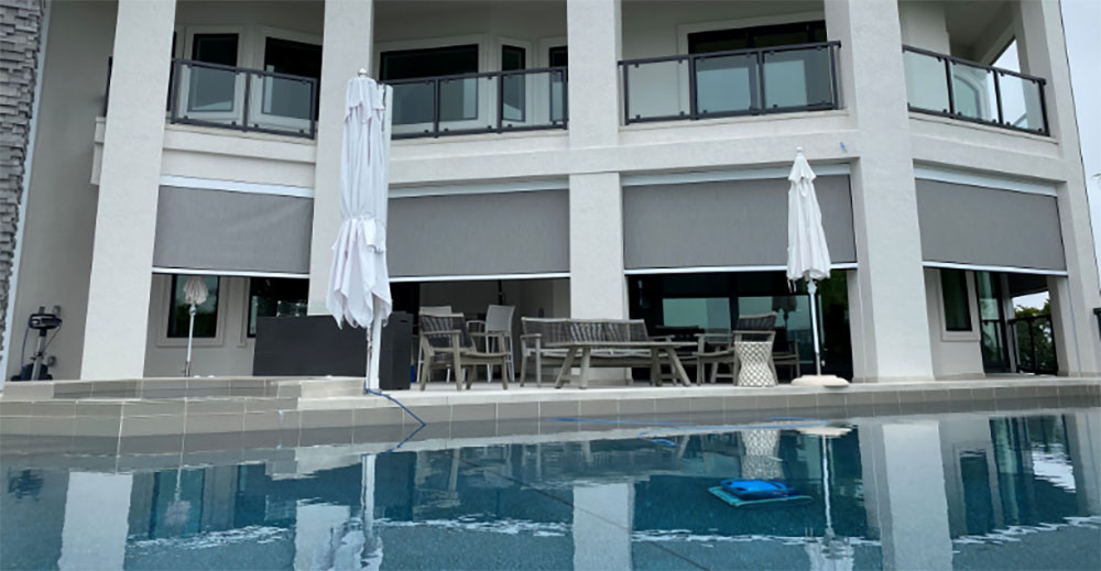 A luxurious outdoor patio with MagnaTrack motorized screens beside a large pool area.