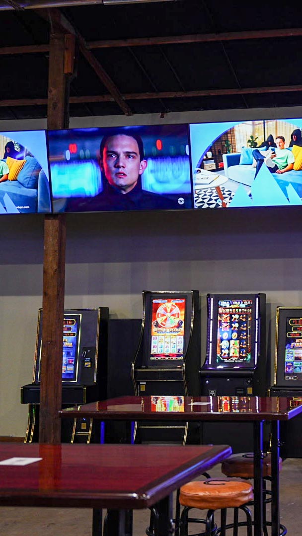 Bar area with slot machines, high-top tables, and multiple TVs showing various programs and sports