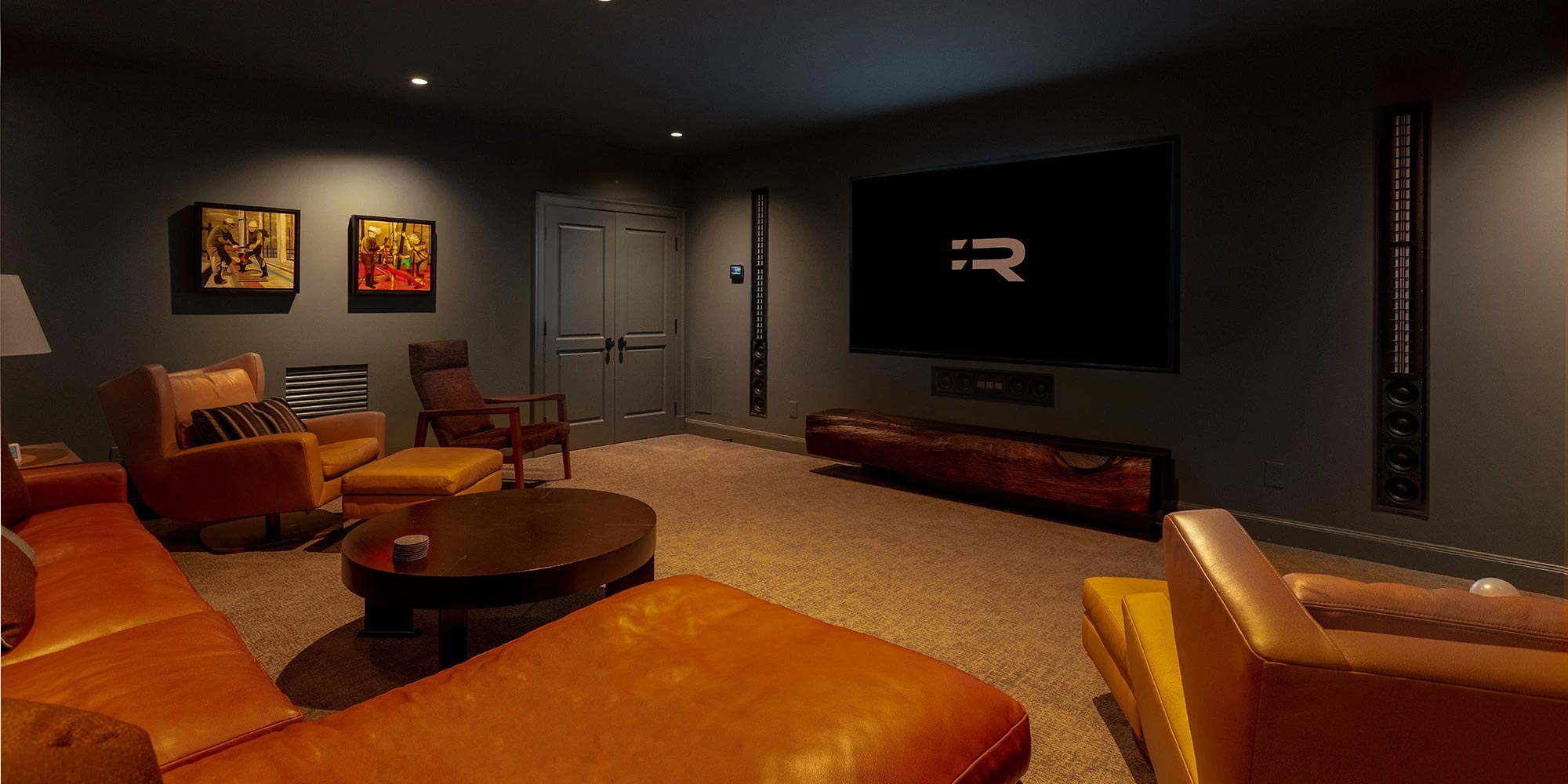 Cozy home theater room with leather seating, wall-mounted speakers, and large screen