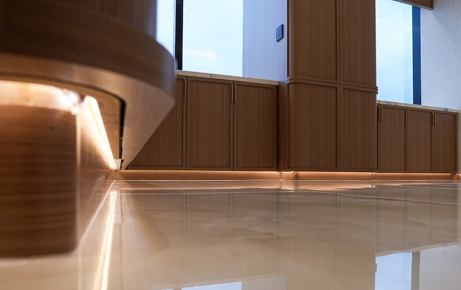 Warm LED toe-kick lighting under walnut cabinetry reflects on a polished marble floor in a luxury interior.