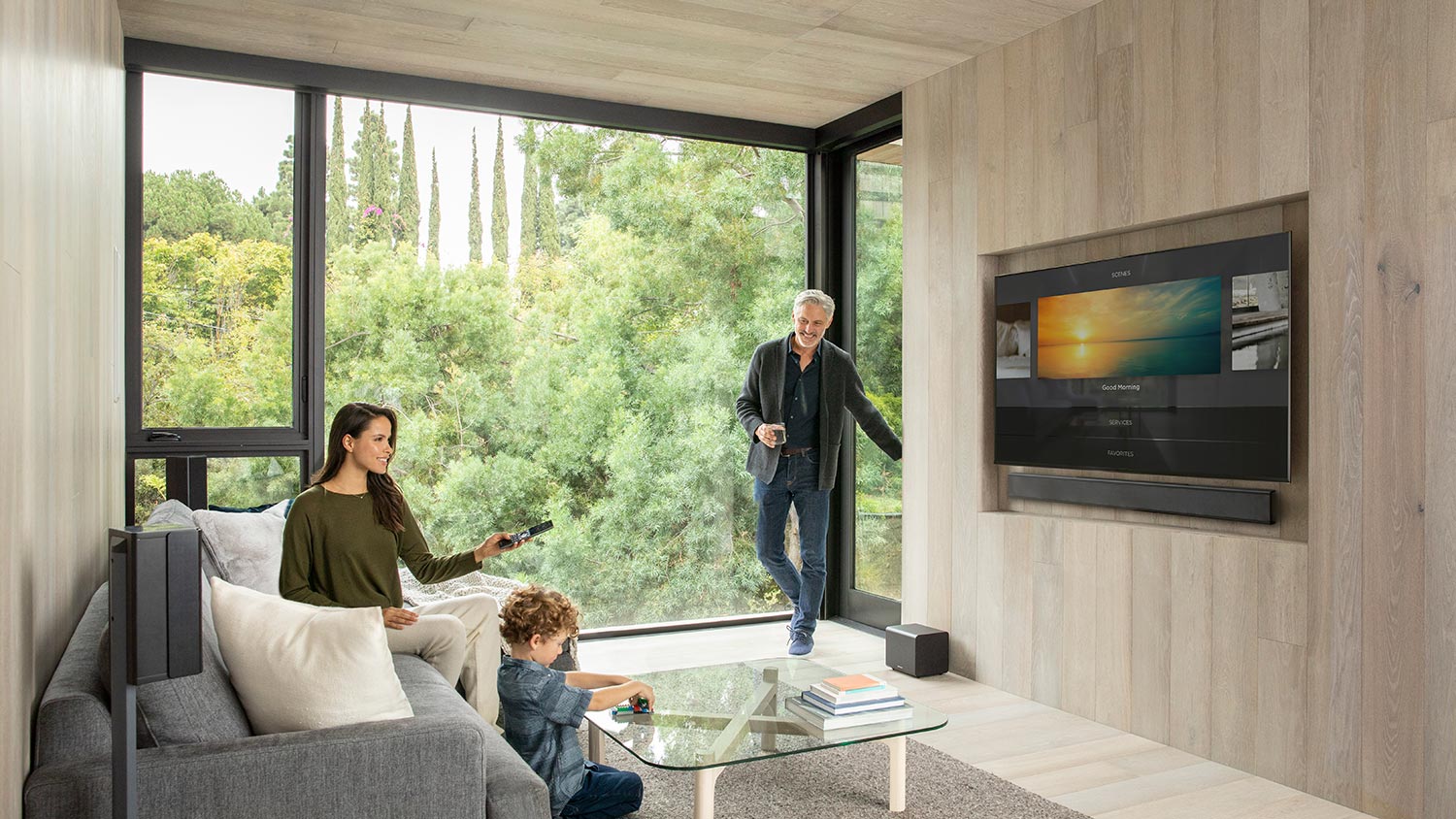 Family in modern living room using smart home system with large TV and floor-to-ceiling windows