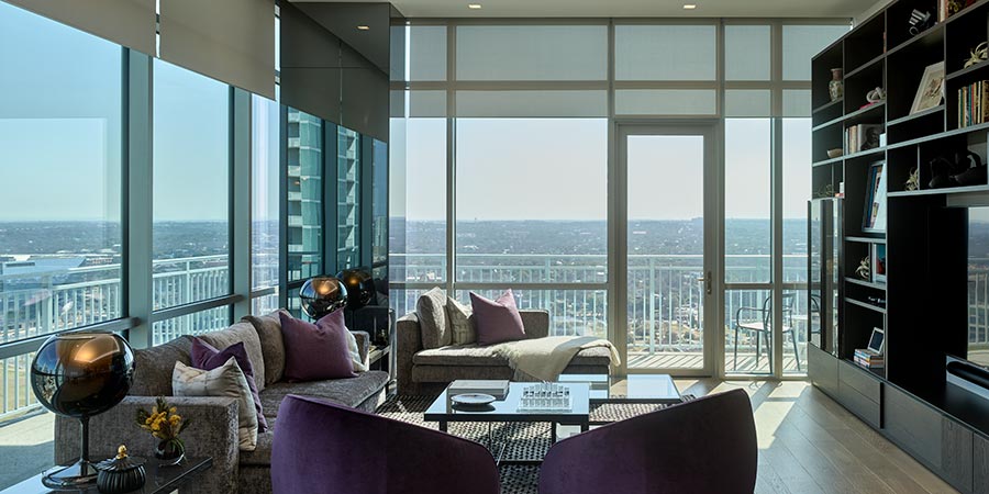 High-rise living room with large windows, sheer roller shades, and views of a cityscape