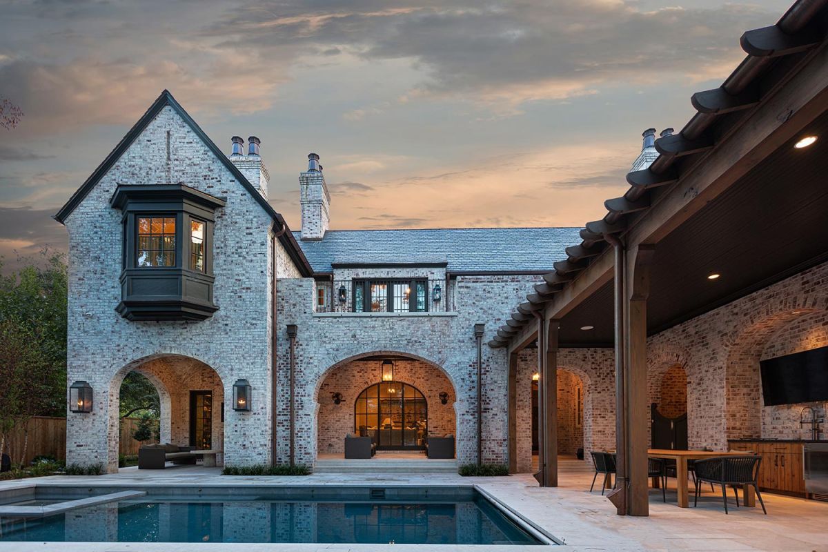Rear view of brick mansion with arches, pool, and outdoor living area