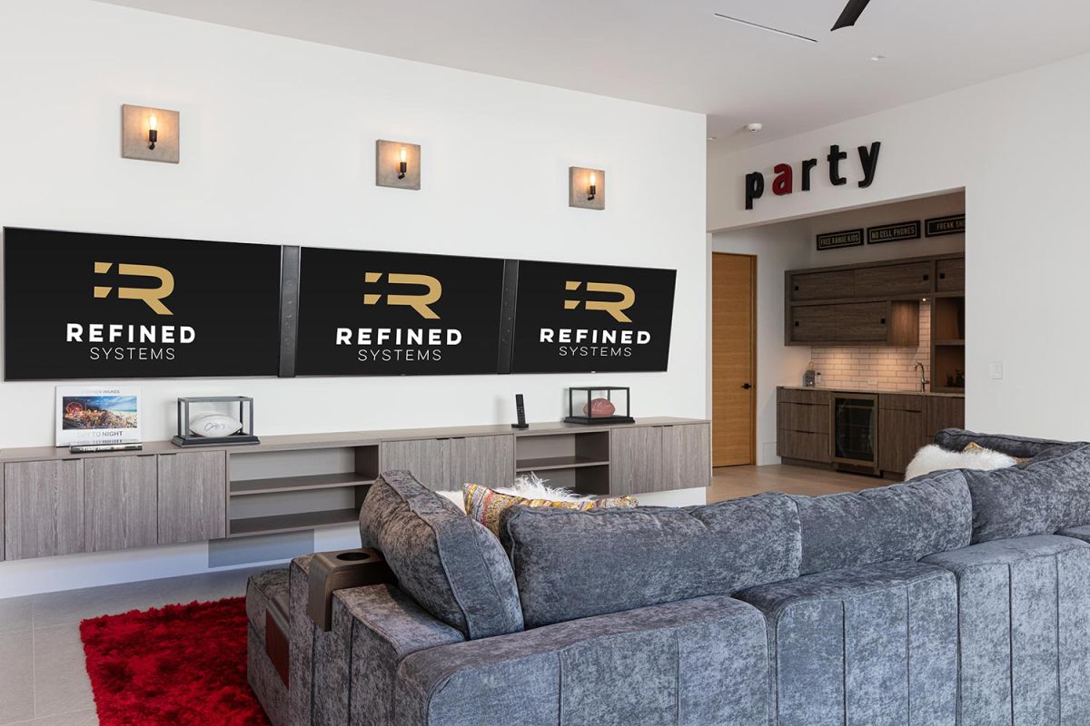 Game room with triple TV setup and gray sectional couch