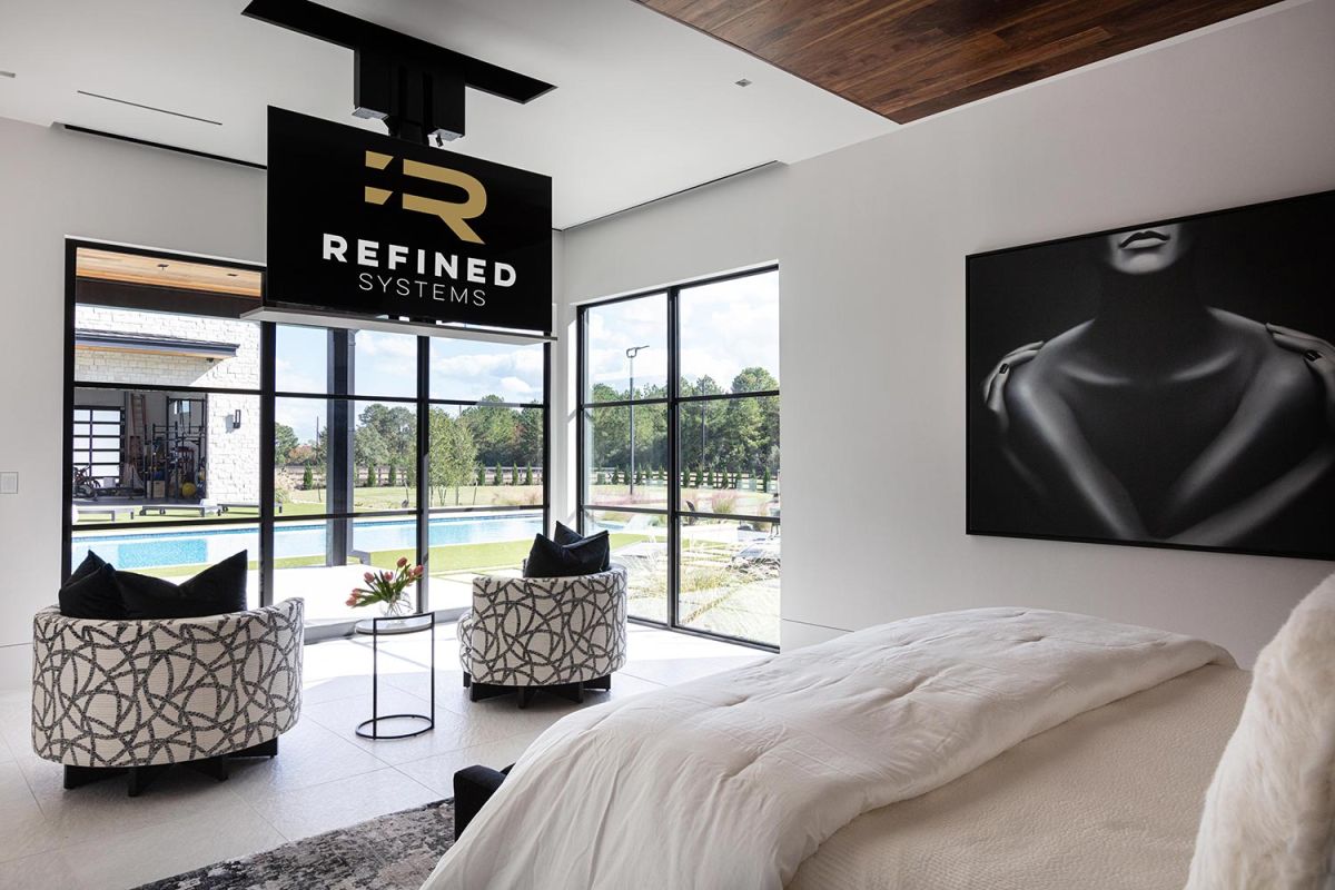 Bedroom with TV on ceiling lift and large windows overlooking pool