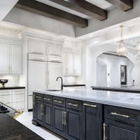 A luxurious modern kitchen with a large island, elegant lighting fixtures, white cabinetry, and gold accents.