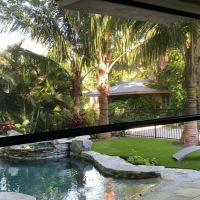 patio screen partially lowered over a pool and palm tree backyard with stone patio and lounge chair