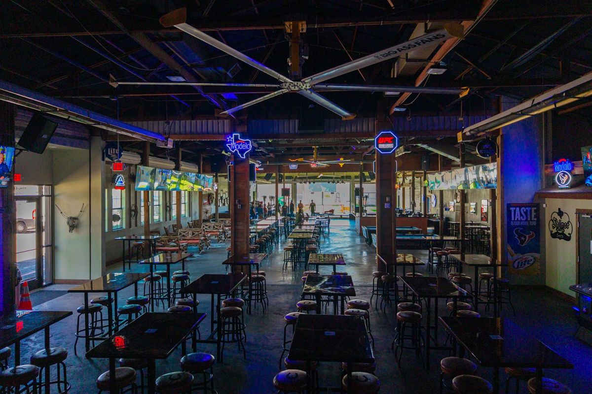 Dimly lit bar interior with rows of tables, stools, and ceiling fans