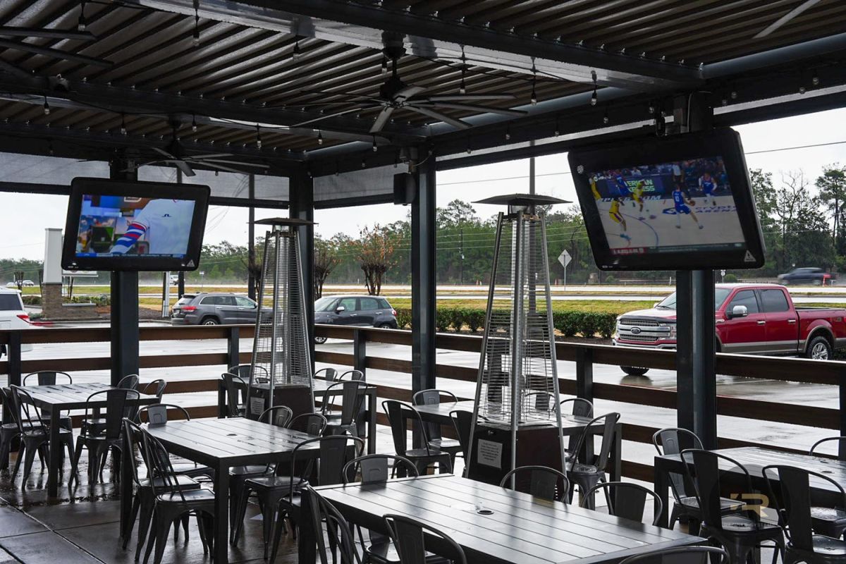 Outdoor patio with mounted TVs showing sports, patio heaters, and metal tables with chairs.