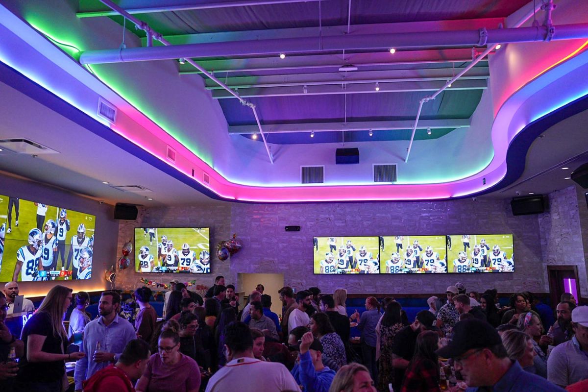 Lively bar scene with sports screens and multicolored LED ceiling lighting.