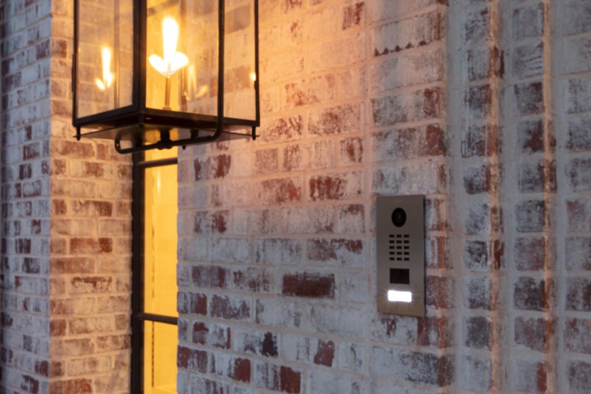 Wall-mounted lantern sconce next to modern door intercom on brick exterior