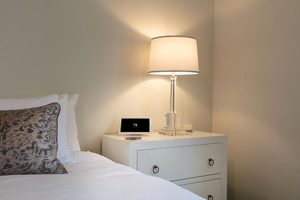 Nightstand with clear lamp, smart panel, and pillow-covered bed