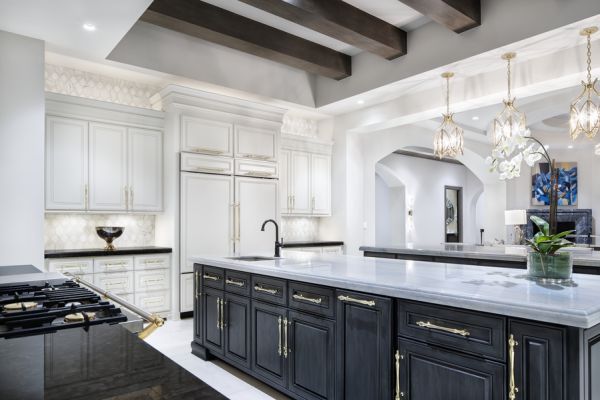 A luxurious modern kitchen with a large island, elegant lighting fixtures, white cabinetry, and gold accents.