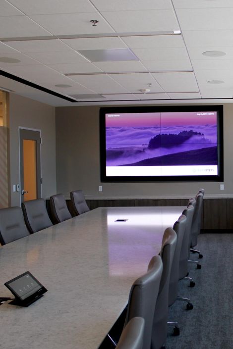 Modern conference room with a large wall-mounted screen displaying a scenic image, surrounded by leather chairs and a marble table