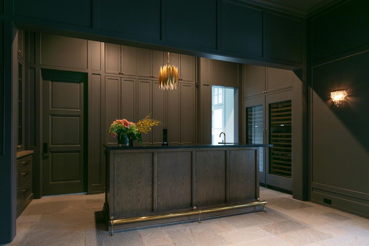 Stylish home bar with dark cabinetry, floral arrangement, and gold pendant