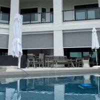 A luxurious outdoor patio with MagnaTrack motorized screens beside a large pool area.
