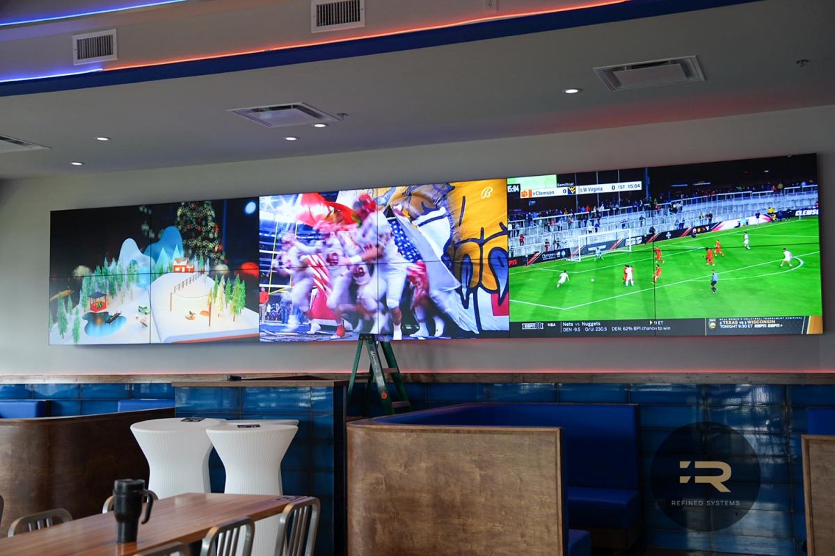 Indoor bar wall with multiple large screens showing different sports broadcasts.