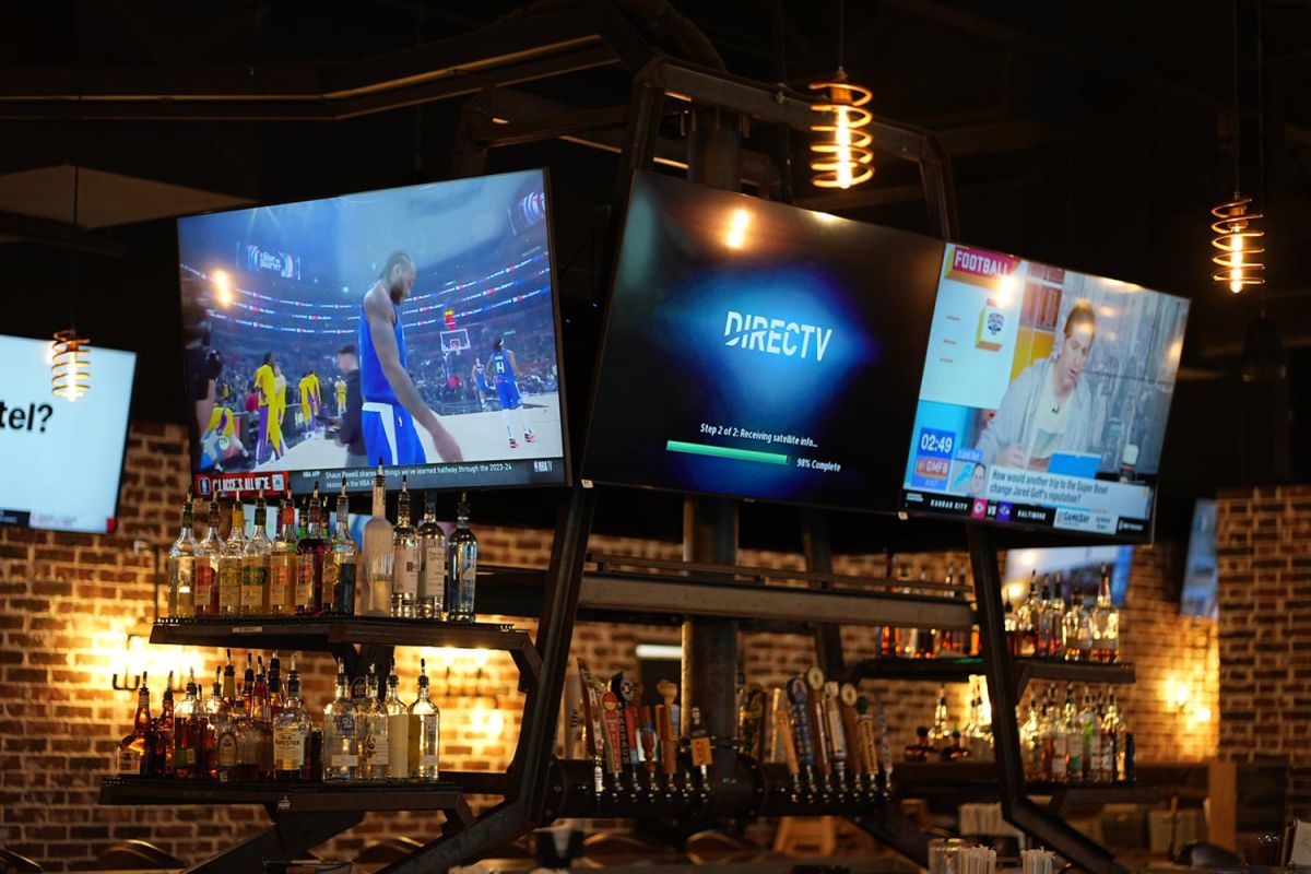 TVs above a bar showing basketball, satellite feed setup, and a sports news segment.