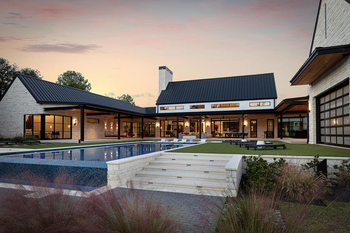 Modern estate backyard at dusk featuring pool and stone patio