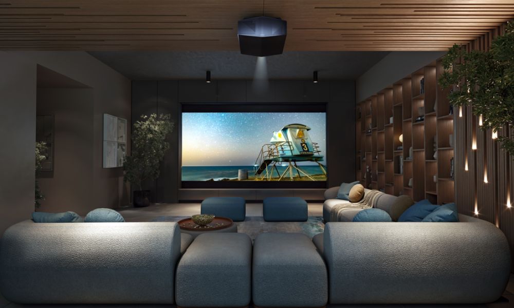 <span class="uk-h4">Luxury home theater room with plush blue seating, a large projection screen displaying a beach scene, wood-accented walls and ceiling, and soft ambient lighting.</span>