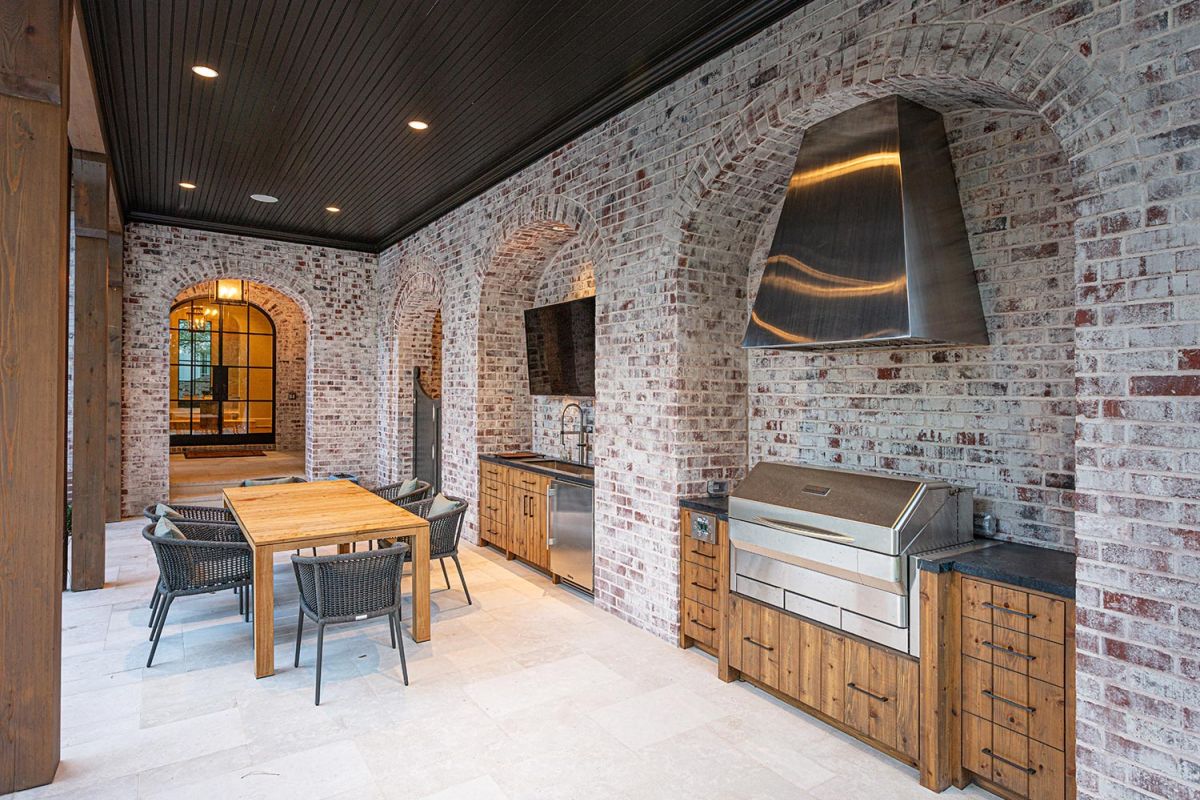 Covered outdoor kitchen with grill, hood, and brick archways