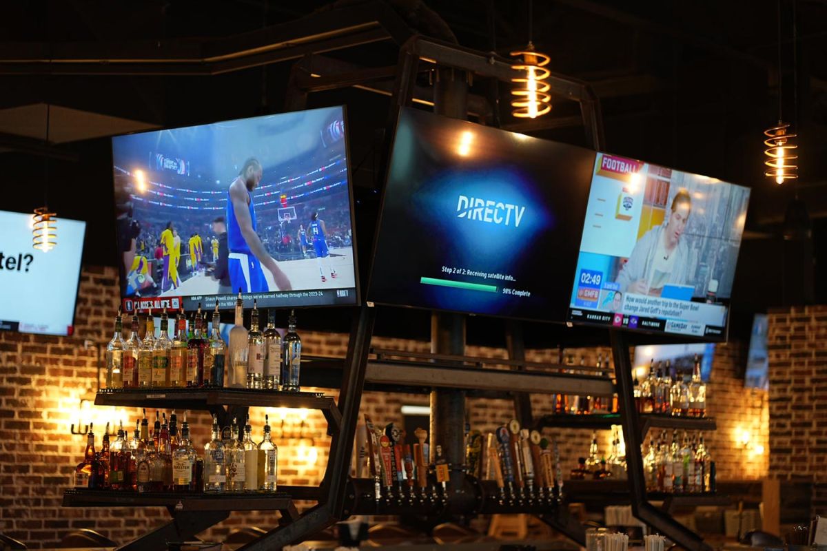 TVs above a bar showing basketball, satellite feed setup, and a sports news segment.