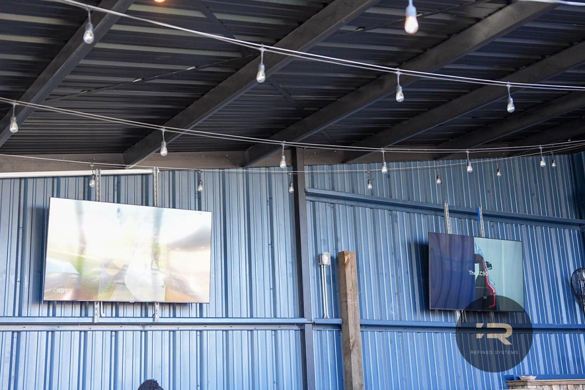 Wall-mounted TVs on a covered patio with string lights and a metal ceiling.