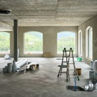 Interior of a building under construction with ductwork, ladder, and open windows showing green hills and blue sky outside.