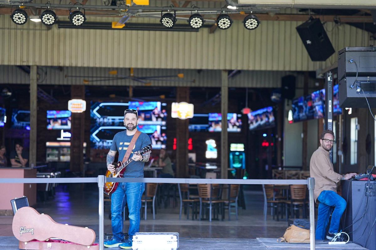 Man with electric guitar performing in a venue with stage lights and TVs